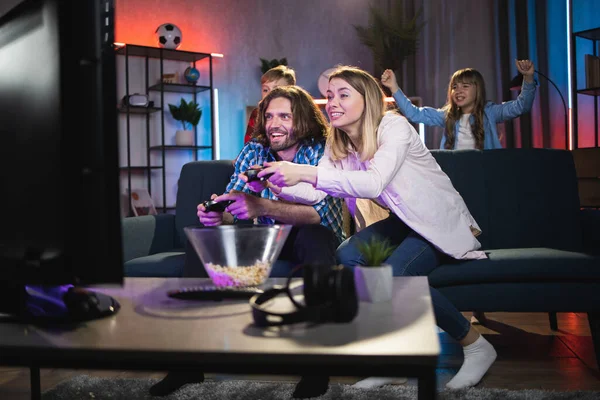 Ouders spelen videospelletjes terwijl kinderen hen aanmoedigen — Stockfoto