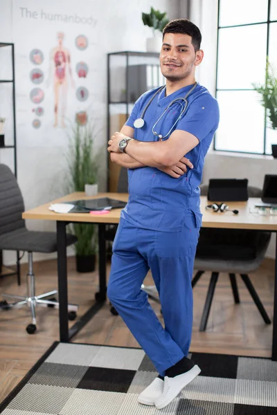Arabian male doctor posing with arms folded in modern light clinic office