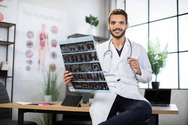 Medico arabo malese radiologo, appoggiato sul tavolo, e con una tomografia a raggi X — Foto Stock