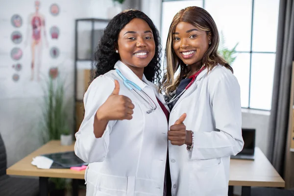 두 명의 아리따운아 프로 미국 여성내과 의사들이 웃으며 손을 들고 카메라 앞에 서서 — 스톡 사진