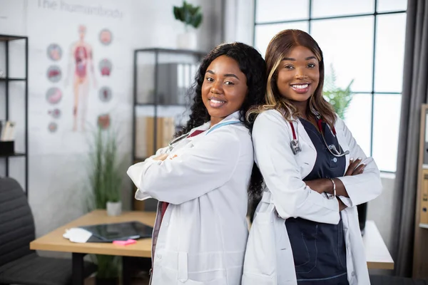 흑인 피부를 가진 아름답고 젊은 흑인 여성 두 명 이 팔을벌린 채 뒤로 서 있는 아프리카 의사들 — 스톡 사진