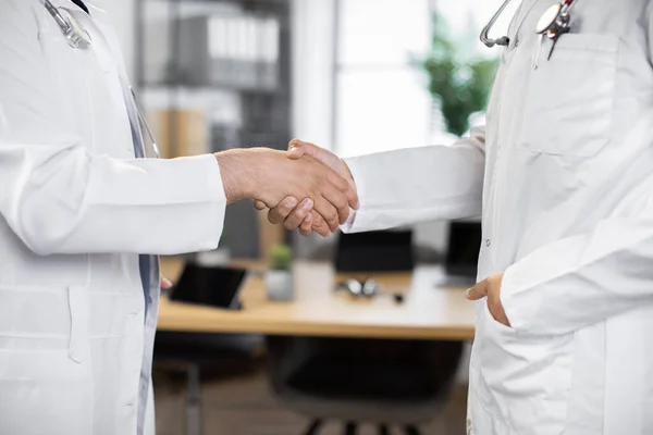 Two unrecognizable male medical practitioners doctors are shaking their hands, close-up.