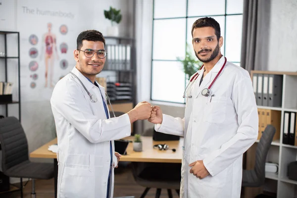 Team of two handsome confident male Arab doctors bumping fists in clinic — Stock Photo, Image