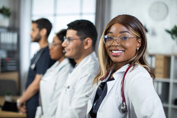 아 프로 - 미국 여성 의사, 병원 방에서 다양 한 인종의 동료들 과 카메라 앞에서 웃고 있다. — 스톡 사진