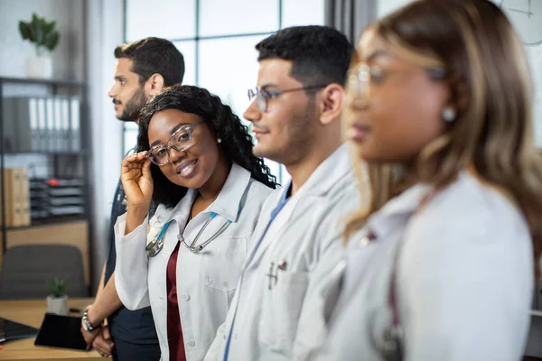 Profilporträtt. Multiracial grupp av fyra läkare i labbrockar stående i rad. — Stockfoto