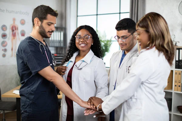 Unity och lagarbete koncept där fyra läkare och sjuksköterskor i ett medicinskt team stapla händerna tillsammans — Stockfoto