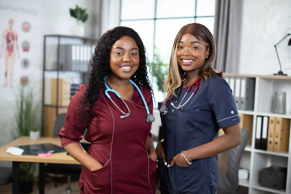 Two female African American doctors in colorful medical scrubs, smiling in modern hospital room