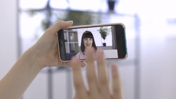 Вид на спину жіночих рук, що тримають телефон та вітають махаючого друга на онлайн-відеодзвінок . — стокове відео