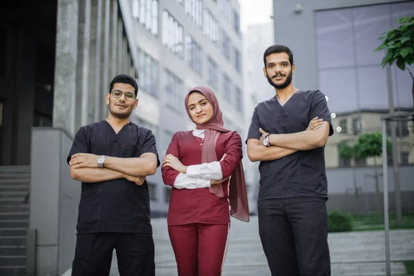 Three young confident multiethnic doctors, standing outside the hospital and looking at camera — Stock Photo, Image
