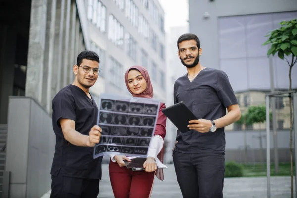 Drei Ärzte, eine Frau im Hijab und zwei Männer in medizinischer Kleidung diskutieren über die Röntgenuntersuchung der Patienten — Stockfoto