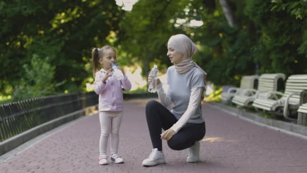 Арабская мать смотрит на свою дочь и питьевой воды во время отдыха после спортивных тренировок на открытом воздухе — стоковое видео