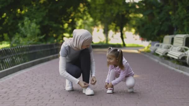 Madre araba e sua figlia che aggiustano le scarpe da ginnastica, sedute sulla pista da jogging nel parco — Video Stock