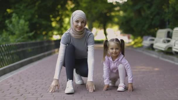 Активная мусульманская семья, мама и дочь, на коленях, готовые к пробежке по парку — стоковое видео