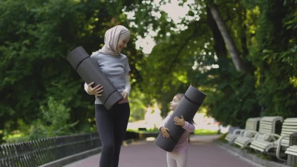 Muslim mother and her cute 4-aged daughter, posing at camera in summer park, holding yoga mats — Stock Video