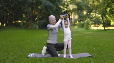 Müslüman anne, küçük şirin kızına halterlerle egzersiz yapmayı ve eğlenmeyi öğretiyor.