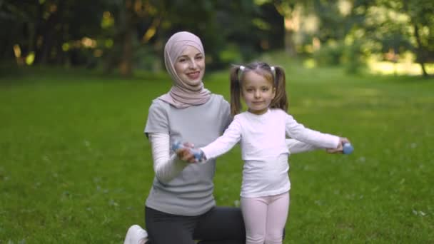 Tiro al aire libre de niña feliz levantando pesas bajo la supervisión de su madre deportiva — Vídeo de stock