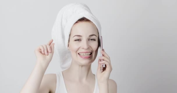 Biała kobieta z ręcznikiem na głowie, bawiąca się podczas tańca z telefonem w rękach — Wideo stockowe