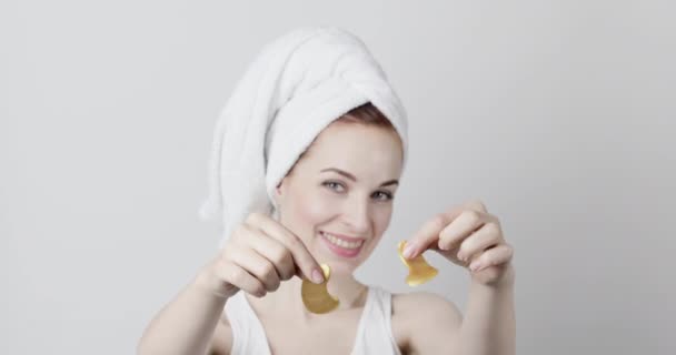 Glimlachende vrouw met haar gewikkeld in handdoek, poseren met gouden onder ogen vlekken in handen. — Stockvideo