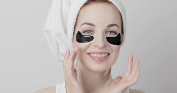 Joyful woman removes black collagen hydrogel pads mask, isolated on light gray background — Stock Video