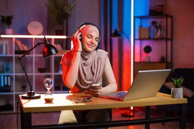 Arap kadın cep telefonu tutuyor ve kulaklıkla müzik dinliyor.