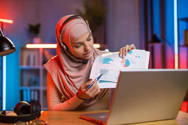 히잡을 입은 이슬람 아가씨는 노트북에서 비디오 채팅 모임을 통해 다른 차트와 그래프를 설명하고 있다. — 스톡 사진