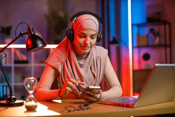 히잡을 입은 아랍 여성, 헤드폰으로 음악을 즐기며, 전화번호부에서 노래를 선택하는 모습 — 스톡 사진
