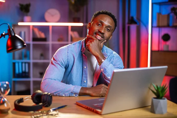 Confident black guy sitting at desk with wireless laptop