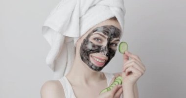 Kömür soyan yüz maskesi takan genç bir kadın ellerinde salatalık dilimleri tutuyor.