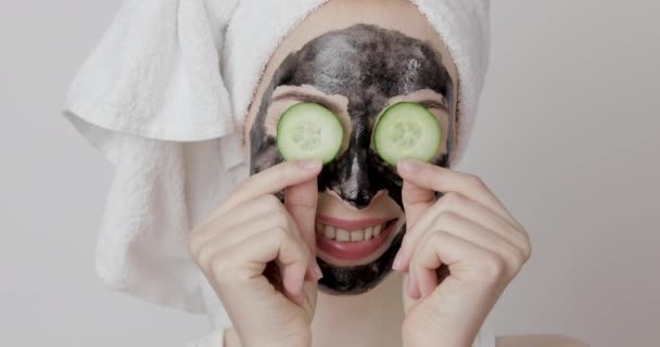 Žena s černým čistícím dřevěným uhlím obličejová maska, drží okurkové plátky na očích — Stock video