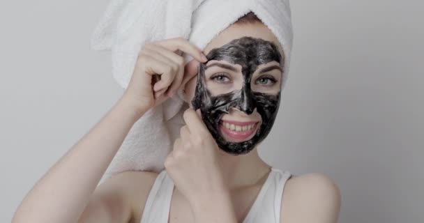 Hezká žena odstraňuje carbo černou peel-off masku z obličeje, na bílém pozadí — Stock video