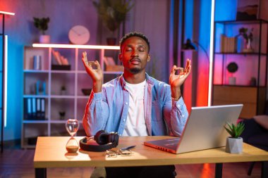 Afrikalı adam iş yerinde gözleri kapalı meditasyon yapıyor.