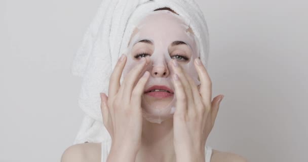 Young lady in towel on her head, wearing sheet facial mask for moisturizing skin — Stock Video