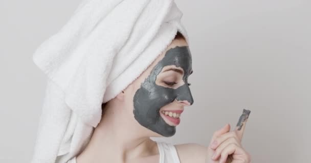 Chica con una toalla en la cabeza, la aplicación de máscara de arcilla facial y tratamientos de belleza en su cara — Vídeos de Stock