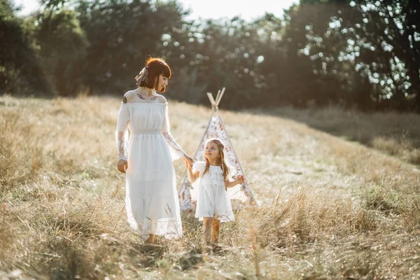 Joyeux petite fille marchant à l'extérieur dans le champ avec sa mère. Wigwam sur le fond. — Photo