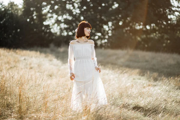 Boho menina em vestido branco, com penas no cabelo e flash tatuagens de pé e olhando para longe — Fotografia de Stock