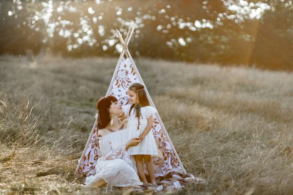 Gelukkig indiaan vrouw met haar kleine dochter knuffelen en kijken elkaar in de buurt tipi tent — Stockfoto