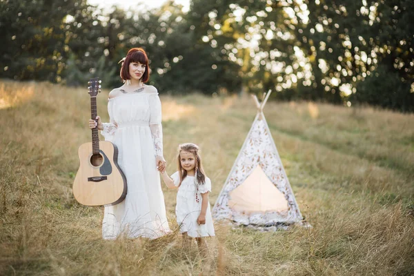 Mãe e filha nativa americana em vestidos de boho, posando para câmera com guitarra no campo — Fotografia de Stock