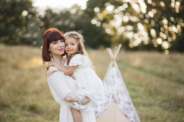 Мама хіпі, тримає милу дочку на руках, позує на відкритому повітрі в літньому полі — стокове фото