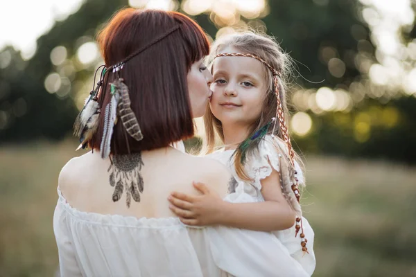 Boho vrouw met droom catcher tatoeage op rug, knuffelen en kussen haar kleine kind in het veld — Stockfoto