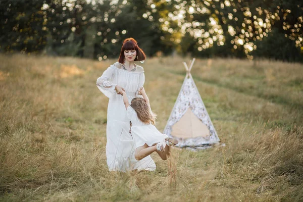 Jovem mãe bonita gira com uma pequena filha em seus braços, desfrutando de belo pôr do sol de verão — Fotografia de Stock