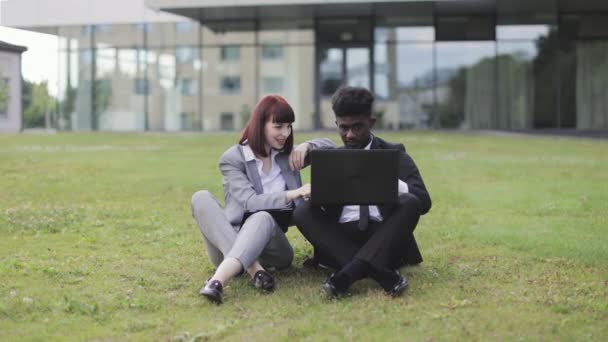 Affärspartners, sitter på gräset utanför kontoret och firar framgång med upphöjda armar — Stockvideo