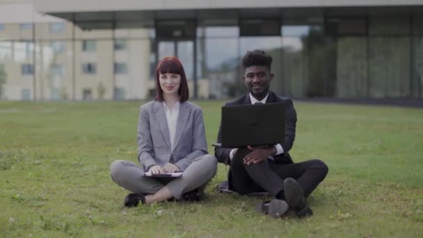 Gente feliz de negocios, sentados en la hierba verde en frente de la oficina, mostrando el éxito con el pulgar hacia arriba — Vídeos de Stock