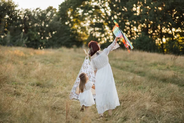 Família feliz mãe e filha, se divertindo juntos no campo selvagem, correndo com pipa colorida — Fotografia de Stock