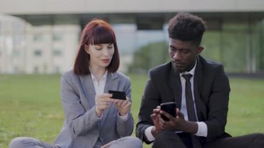 Resmi olarak çok ırklı meslektaşlar ofis dışındaki çimlerin üzerinde oturarak online ödeme yapıyorlar.