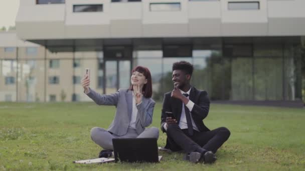 Unga affärskollegor som har roligt utomhus, sitter utanför kontoret och tar en selfie — Stockvideo