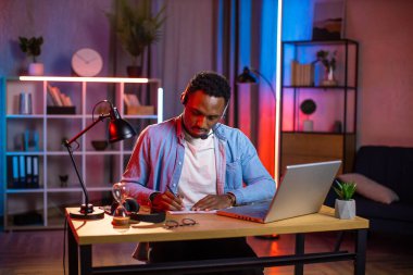 Kulaklık takmış Afrikalı bir adam video görüşmesi sırasında not alıyor.