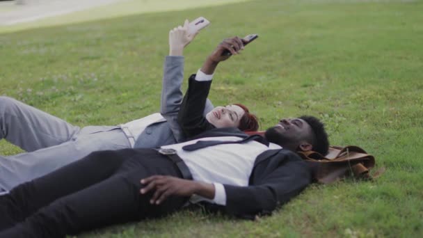 Glückliche Kollegen, die mit Smartphones im Gras liegen und Nachrichten oder soziale Netzwerke verfolgen — Stockvideo