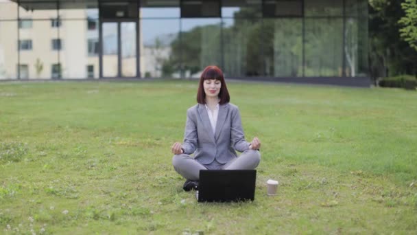 Mujer joven calma relajante meditando, sentado al aire libre en la hierba verde con el ordenador portátil — Vídeo de stock