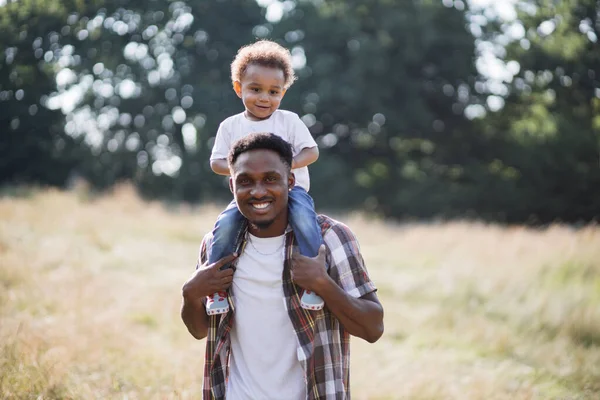 Africano hombre sosteniendo hijo en hombros mientras de pie en campo — Foto de Stock