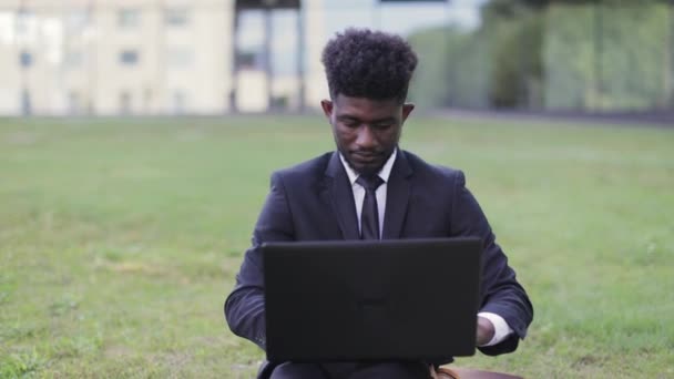 Afroamerikanischer Geschäftsmann sitzt draußen in der Nähe des Büros und gibt den Daumen nach oben, während er Laptop benutzt — Stockvideo